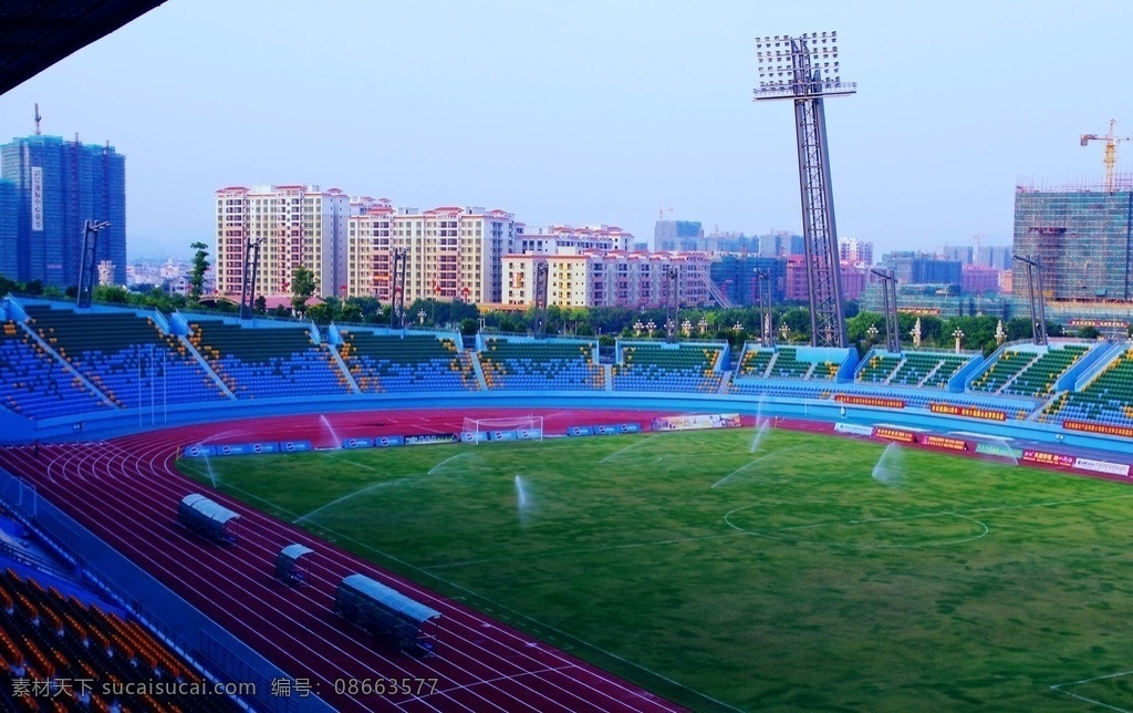 梅县文体中心 曾宪梓体育场 彩色场馆 座席 球场射灯 灯柱 田径跑道 教练坐席 旗杆 绿草球场 高楼建筑 树木天空 国内旅游 旅游摄影